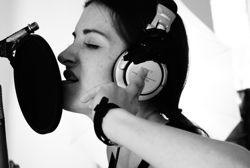 ヘッドホンをつけてマイクに向かって歌う女性のクローズアップ写真