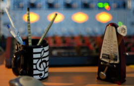 スタジオのデスクに置かれたメトロノームと筆記具入りの音楽柄マグカップの写真