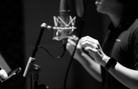 録音ブースでマイクに向かって発声する人物のモノクロ写真