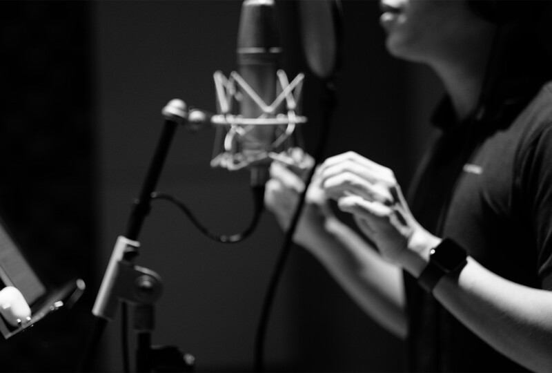 録音ブースでマイクに向かって発声する人物のモノクロ写真