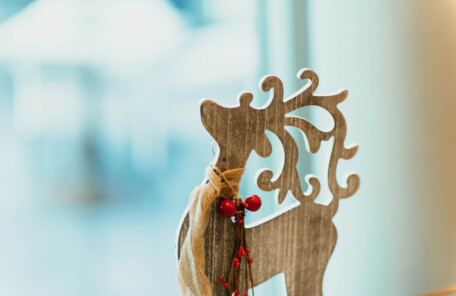 木製のトナカイ型オーナメントに赤い実の装飾が付けられ、背景がぼかされた室内の様子