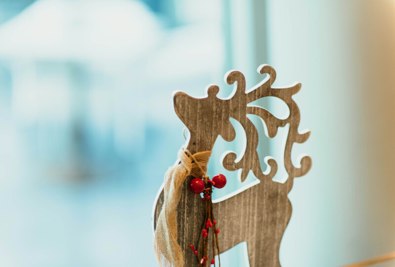 木製のトナカイ型オーナメントに赤い実の装飾が付けられ、背景がぼかされた室内の様子