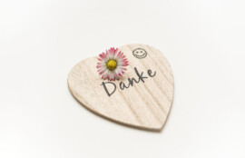 白い背景の上に、花が添えられ「Danke」と書かれた木製のハート型プレートが置かれている様子