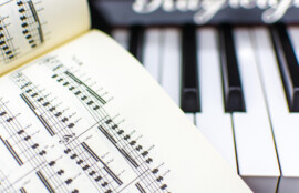 開かれた楽譜と、その奥に並ぶキーボードの鍵盤が写ったクローズアップ