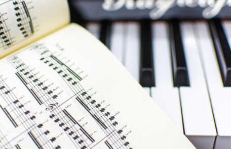 開かれた楽譜と、その奥に並ぶキーボードの鍵盤が写ったクローズアップ