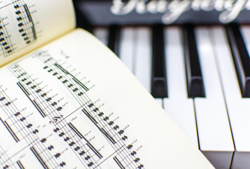開かれた楽譜と、その奥に並ぶキーボードの鍵盤が写ったクローズアップ