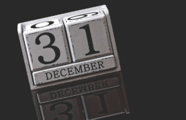 「31 DECEMBER」と表示された卓上カレンダーが暗い背景の前に置かれ、下部に反射が写り込んでいる様子