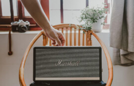 椅子の上に置かれたMarshallのポータブルスピーカーを手で持ち上げるシーン