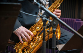 マイクスタンド越しにサックスを構える演奏者の手元を捉えた写真