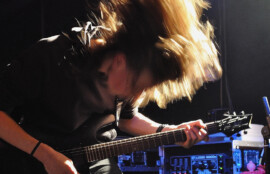 ステージ上で激しくギターを弾く長髪のギタリスト