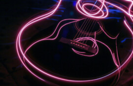 暗い背景に、ピンクの光跡でギターの輪郭が描かれた抽象的な写真