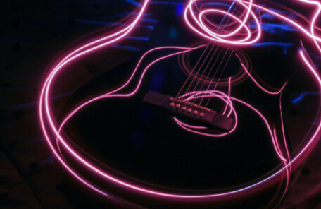 暗い背景に、ピンクの光跡でギターの輪郭が描かれた抽象的な写真