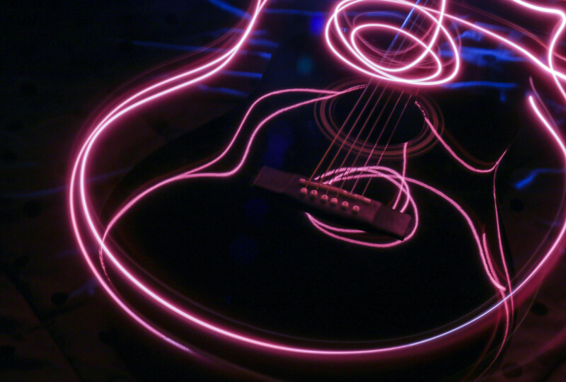 暗い背景に、ピンクの光跡でギターの輪郭が描かれた抽象的な写真
