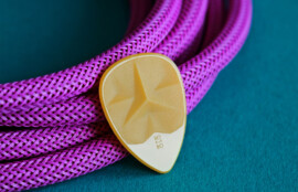 ターコイズの布の上に紫の編み込みケーブルとベージュのギターピックが置かれた接写