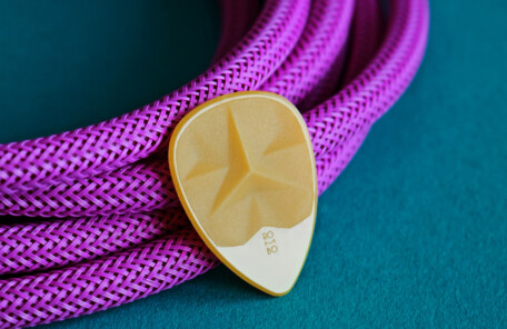 ターコイズの布の上に紫の編み込みケーブルとベージュのギターピックが置かれた接写