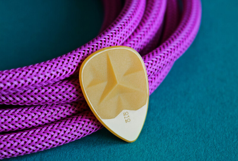 ターコイズの布の上に紫の編み込みケーブルとベージュのギターピックが置かれた接写